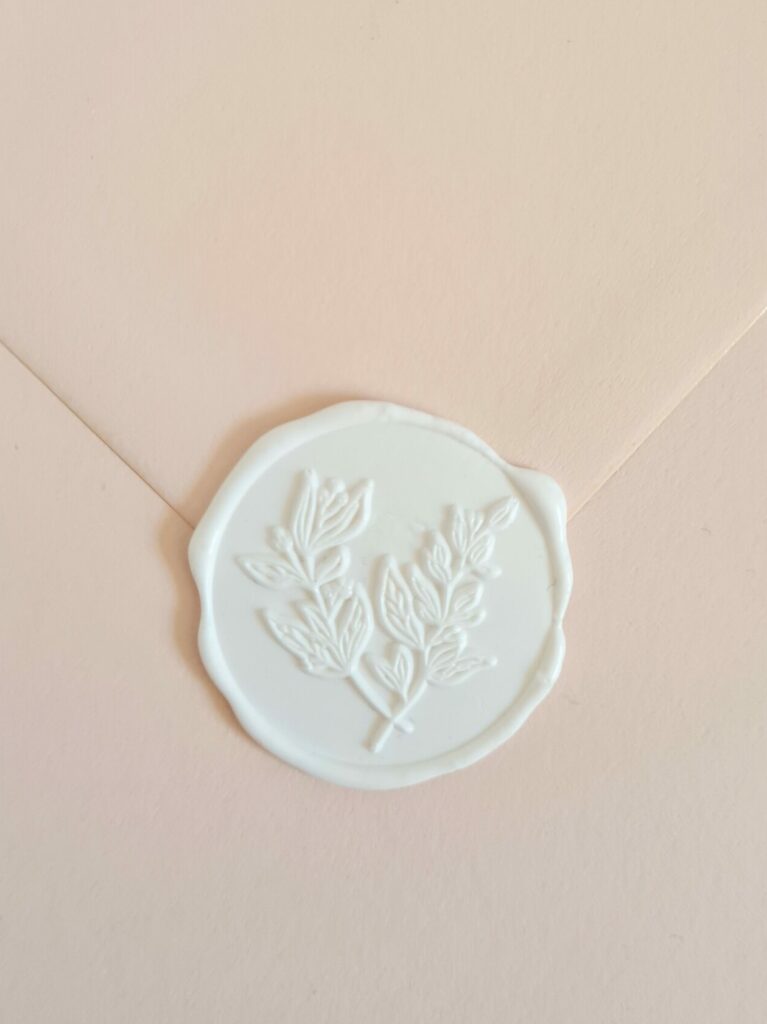 A nude-coloured envelope sealed with a white wax seal featuring botanical leaf detailing.