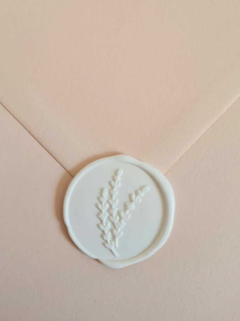 A nude-coloured envelope sealed with a white wax seal featuring foliage leaf detailing.