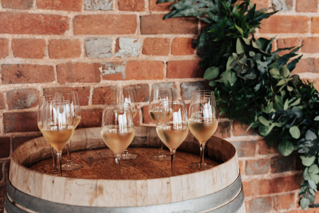 An image of Brickhouse Vineyard's white wine poured in glasses, placed on top of a wooden wine barrel inside the red brick roundhouse. The glasses are filled with the golden-hued wine, ready to be enjoyed by guests in the rustic and charming atmosphere of the venue.