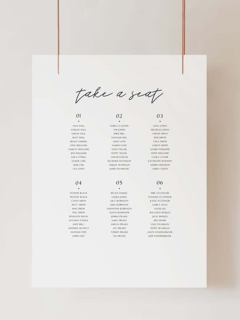 An image of a black and white seating plan sign featuring modern calligraphy-style text that reads "take a seat" with 6 table numbers and guests listed below. The sign is hanging on ribbon with a beige background behind.