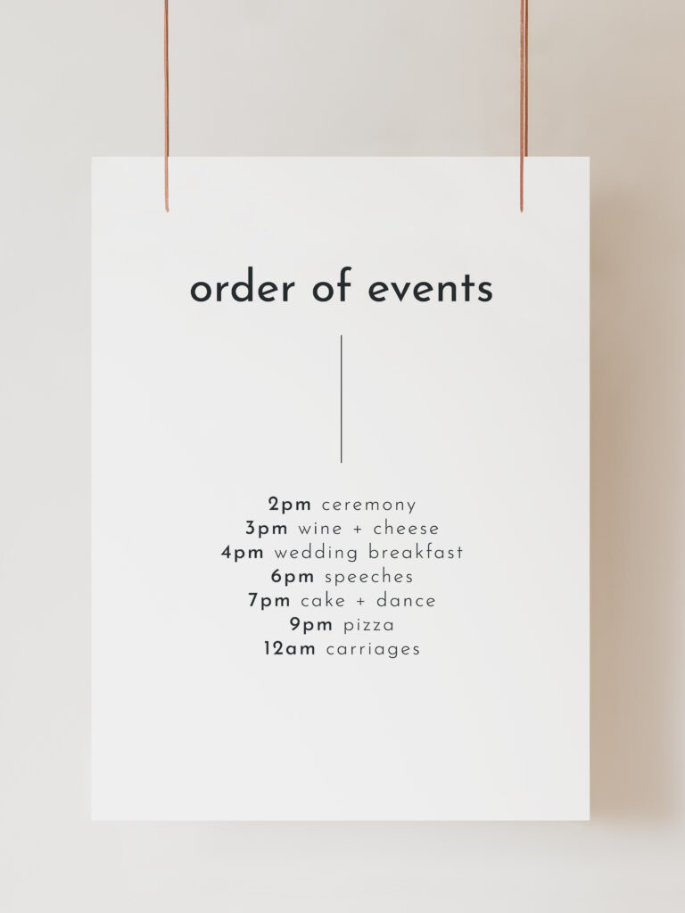 A white wedding Order of the Day sign with modern black text reading "Order of Events" with timings and events listed below. The sign is hanging on ribbon with a beige background behind.