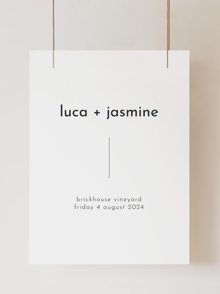 A white wedding welcome sign with modern black text reading "luca and jasmine brickhouse vineyard" with the wedding date listed below. The sign is hanging on ribbon with a beige background behind.