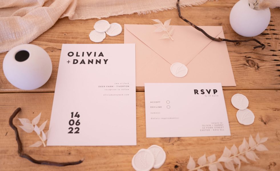 A flat lay image of a black and white wedding invitation suite featuring an invitation card, RSVP card, wax seals, and a beige envelope. The black and white invitation cards have elegant typography and a minimalist design. The wax seals have botanical detailing and add a decorative touch to the suite.