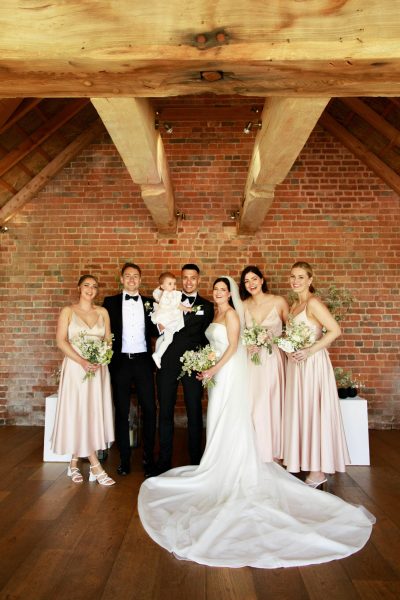 A photo of the bridal party, alongside the bride and groom, standing inside the rustic barn at Brickhouse Vineyard in Devon. The group is gathered in a joyful moment, and the rustic barn interior adds to the warm and inviting atmosphere of the scene.