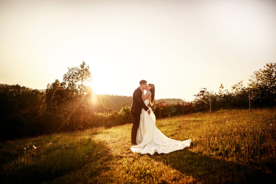 A beautiful photo captures the bride and groom sharing a romantic kiss in a field within the grounds of Brickhouse Vineyard in Devon. The backdrop features a stunning golden hour sunset, creating a warm and enchanting atmosphere for this intimate moment.